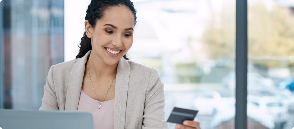 A smiling woman holding a credit card and working on her laptop. Image for the article 'Paying Professionals through Tempfind.'