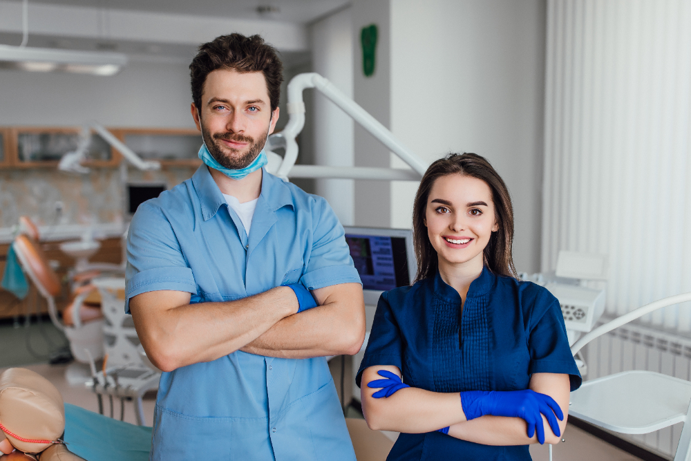 two dental hygienists smiling while standing and wearing their scrub suits